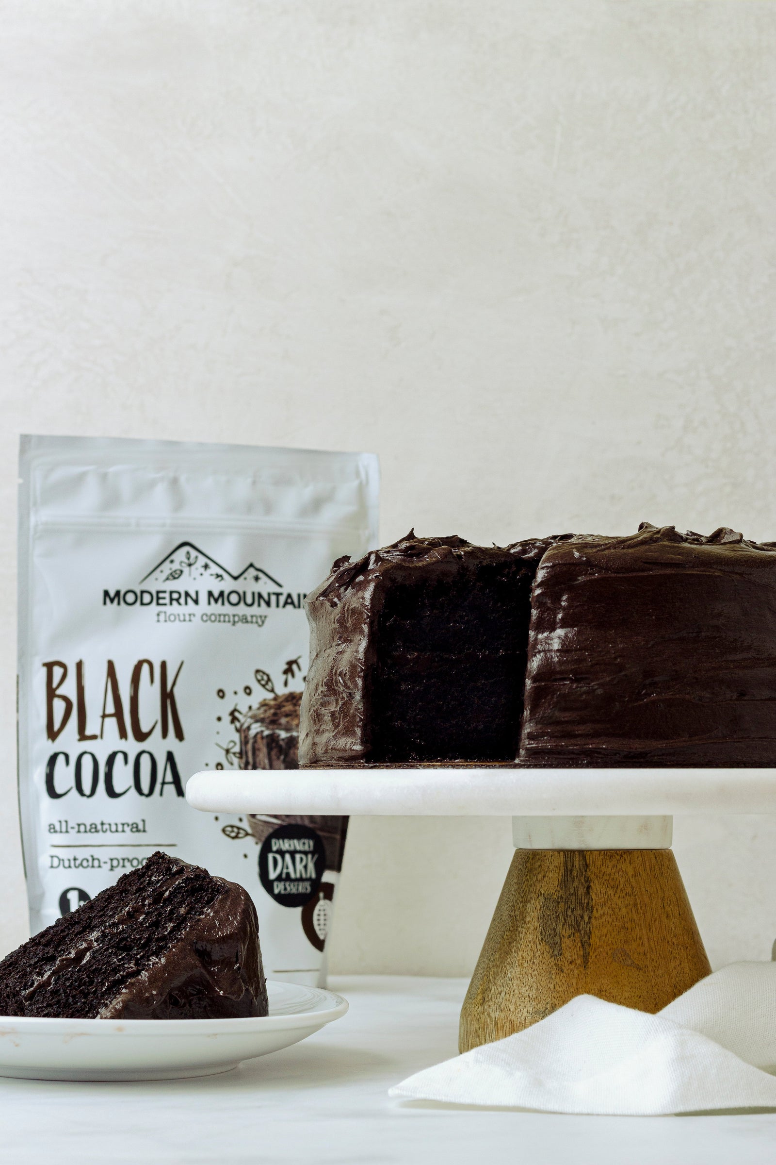 Modern Mountain Black Cocoa pouch beside a dark chocolate layer cake