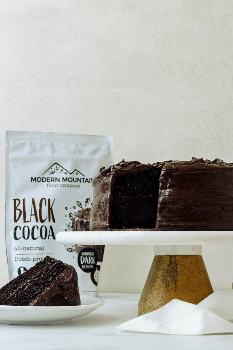 Modern Mountain Black Cocoa pouch beside a dark chocolate layer cake