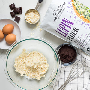 Modern Mountain Lupin Flour and Black Cocoa Powder next to a bowl of flour, eggs, and chocolate